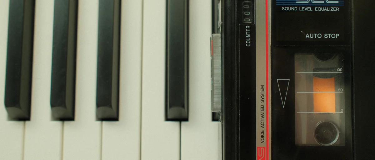 A pocket cassette recorder lying across the keys of the piano, its tape half wound